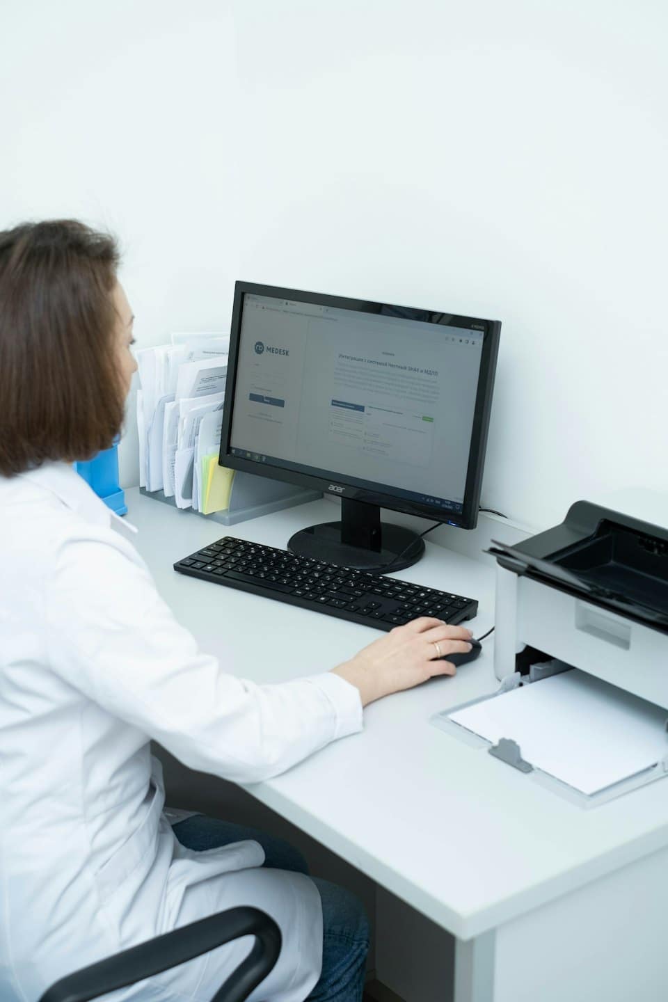 Profesional médico trabaja en una computadora en una oficina concurrida.