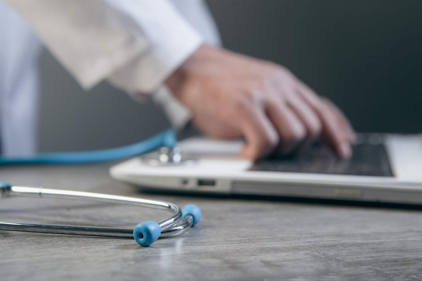 Médico escribiendo en un portátil con un estetoscopio sobre el escritorio.
